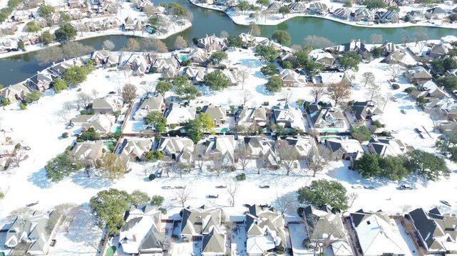 Canal waterways curve past residential lots near Andrew Brown Park East in DFW suburbs. Crisp snowfall coats multi gabled rooftops, waterfront backyards across Coppell, Texas