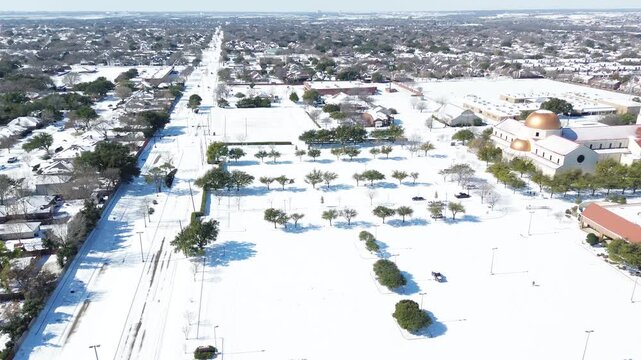 Sprawling St Ann Catholic Parish grounds border East Sandy Lake Road across DFW suburbs. Fresh snowfall envelopes vast parking plazas, landscaped tree groves throughout Coppell, Texas