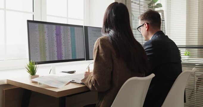 Colleagues analysts accountants teamwork analysis spreadsheet data computer. Two professionals review finance reports on monitors in an office. Clear concept of collaborative financial analysis.