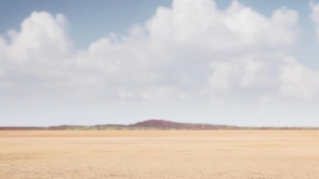 A wide view of a dry landscape with a clear blue sky. The terrain shows cracked earth and some hills can be seen far away. Clouds are present in the background during daytime.