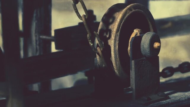 A close view of an old pulley system located in a workshop near a construction site. The pulley shows signs of age and wear. The chain hangs down, indicating its use.
