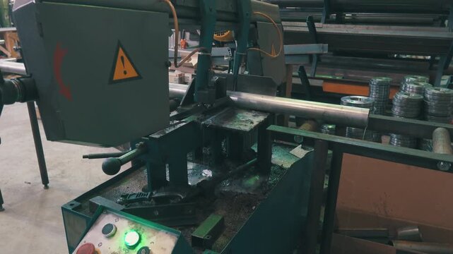 Automatic Band Saw Cutting Metal Pipe: Industrial Machine with Control Panel and Coolant | Steel Tube Fabrication in Factory Workshop | Warning Sign and Stored Metal Fittings on Shelves
