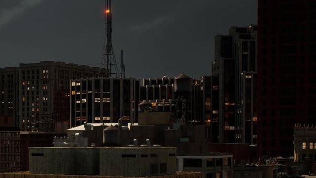 Buildings in a city are visible at night with lights on in windows. A tall tower with antennas stands in the background. The scene shows urban life after sunset with dark skies.