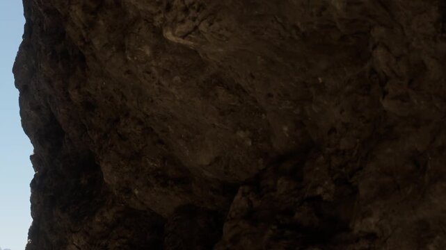 A large rock formation is visible from below in a natural setting. The time is during daylight with a clear blue sky in the background. There are no people present in the scene.
