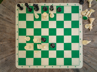 Chessboard game mat with plastic pieces placed on the round wooden table during an outdoor yard leisure recreation activity match. © AncientAftertone