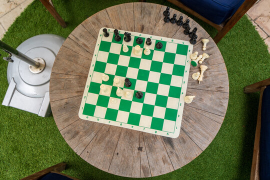 Chess board game with plastic pieces placed on the round wooden table standing on the artificial turf grass ground during the yard match.