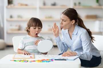Happy Child And Female Therapist Engaged In Speech Therapy Session, Practicing Sounds In Cozy Home...