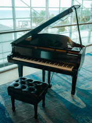 Classical black grand piano with an open lid and a leather tufted bench standing on a blue patterned carpet next to a glass railing. © AncientAftertone