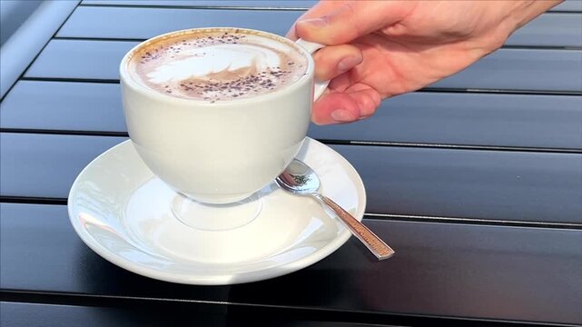 Adult woman reaching for a cup of coffee at an outdoor cafe table, casual coffee break, relaxed leisure, cafe lifestyle, everyday moment.
