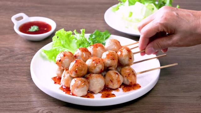 Thai grilled meatballs with sweet and spicy dipping sauce, served on a white plate (Thai street food).	