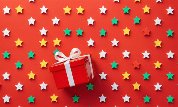 red gift box with white ribbon on red surface covered with multicolored star cutouts