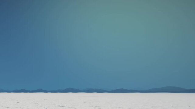 A vast salt flat stretches across the land under a clear blue sky. Distant mountains create a line in the background, showing a wide open space with no people or buildings around.
