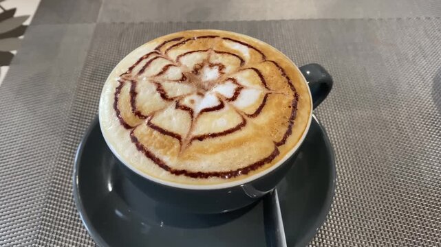 Close up of a hot cup of cappuccino with beautiful chocolate etching syrup flower pattern, representing professional barista skills, cozy coffee shop atmosphere, and morning energy ritual.