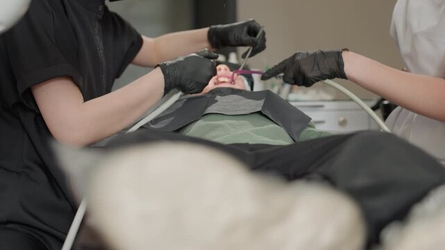 Close up of dental professionals performing orthodontic procedure on patient. Dental tools and equipment visible in clinical setting with soft lighting. Patient lying back