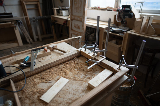 Wooden details of vintage window frame fixed with clamps at workbench in restoration workshop, working process in carpentry studio, worktable with instruments and tools for repair and renovation.