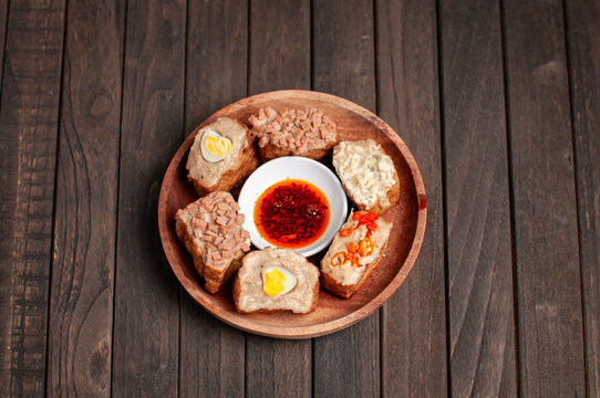 a wooden plate of tahu bakso (tofu stuffed with meat paste) served with various toppings and a dipping sauce.