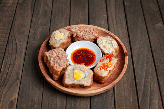 a wooden plate of tahu bakso (tofu stuffed with meat paste) served with various toppings and a dipping sauce.