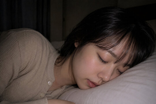 寝室でベージュのボタン付きパジャマを着て枕に頬を置き眠る女性