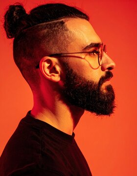 Profile of a bearded man with a man bun and glasses against a vibrant orange background.