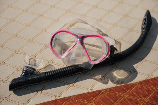 Snorkel equipment resting on patterned boat deck, featuring pink diving mask and black breathing tube for underwater adventure during summer vacation trip, ready for recreation