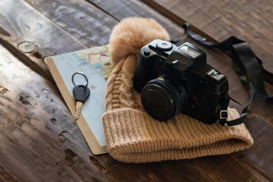 Black camera resting on a knitted beige hat beside a paper map and padlock on a rustic wooden table, suggesting travel planning and adventure.
