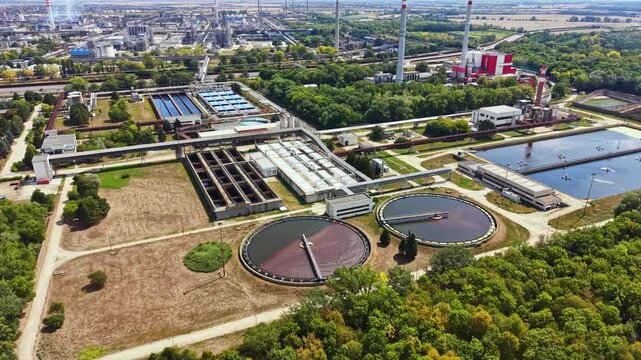 A view of a factory and water treatment facility with several large circular tanks. Green trees surround the area and show a mix of industrial and natural elements.