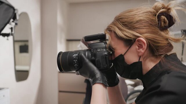 Close up of woman wearing black gloves and holding professional camera focusing intently on taking photographs in indoor studio setting. scene includes visible photography equipment