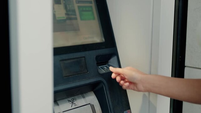 Close-up view of a woman's hand inserting a credit card into an automated teller machine to perform a financial transaction, highlighting modern banking and electronic payment methods