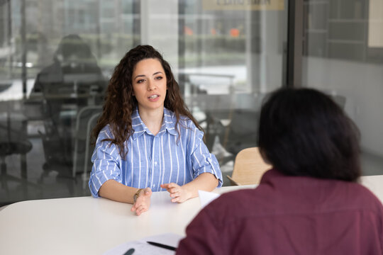 Young adult woman discussing project, planning strategy, speaking with colleague, applicant answers question at office job interview. Recruitment, company staffing, professional business communication