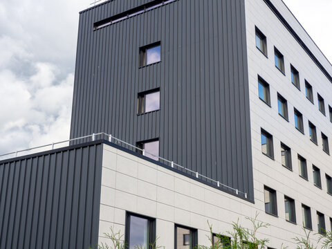Modern multi-story commercial or residential building with a contemporary facade combining dark gray vertical metal cladding and white paneling
