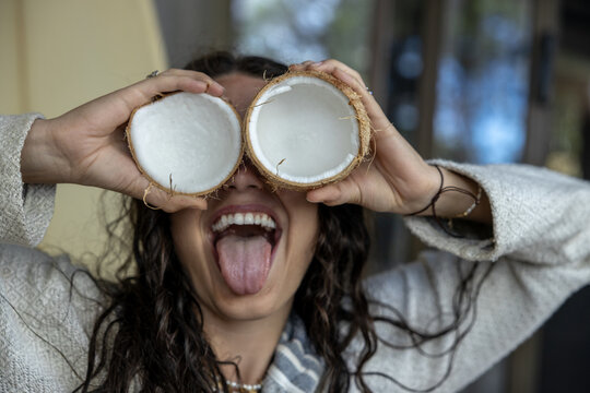 Playful young woman holding coconut halves over her eyes at a tropical resort