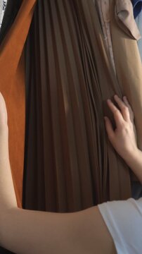 Young woman's hands browsing through a selection of stylish clothes hanging in a closet, carefully feeling the fabrics and considering her options for the perfect daily outfit