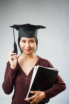 Smiling graduate holding books and graduation cap