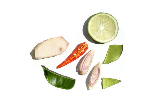 A colorful, close-up pattern of Thai herbs: lime slices, galangal, lemongrass, chilies, and kaffir lime leaves.