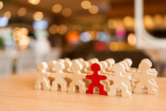 Leadership and talent recruitment concept with one red wooden figure standing out from crowd of people figures on table for unique individuality, team management and business promotion.