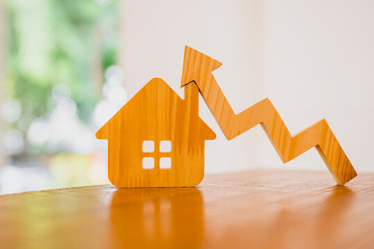 Real estate and property market growth concept with wooden house model and upward trend arrow on table for rising home prices, mortgage investment value and housing appreciation.