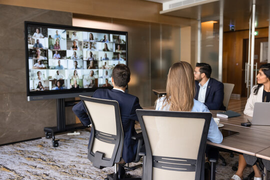 Business team sitting at conference desk, looking at digital monitor displaying diverse people on screen as human resources, virtual meeting event in office. Video call, global communication, recruit