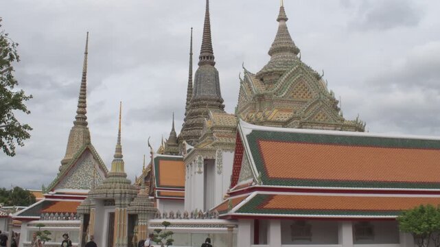 traditional orange-tiled temple roofs and decorative ceramic-tiled spires under a cloudy sky in the sacred courtyard of wat pho bangkok.