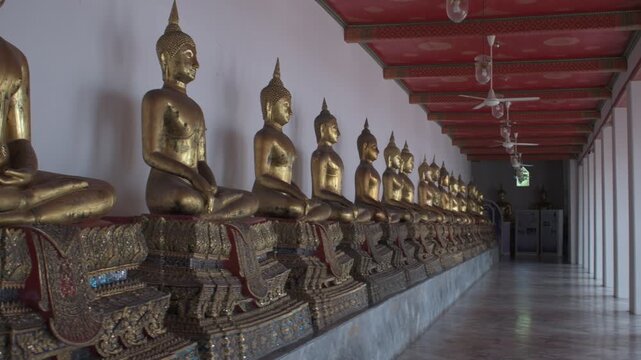a long row of golden seated buddha statues in meditation pose on ornate pedestals along the gallery cloister at wat pho in bangkok thailand
