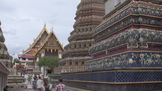 through the temple courtyard past ornate ceramic-tiled stupas and traditional thai temple buildings under an overcast sky at wat pho bangkok