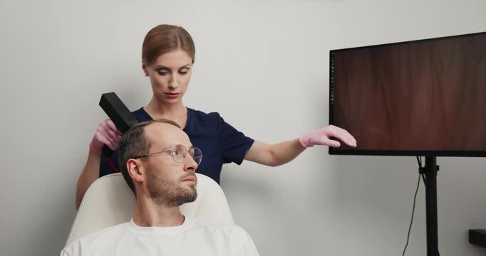Trichologist examining male scalp with handheld digital scanner and magnified hair follicle imaging for clinical diagnosis, concept alopecia for men.