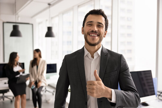 Portrait smiling Middle-eastern businessman giving thumbs up in corporate office, represents business achievement, success and approval, express positive feedback of customer services. HR, employment