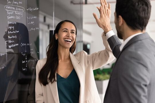 Smiling business colleagues, team members exchanging high-five, celebrating victory, professional success and joint achievement in corporate office. Effective teamwork, collaboration, reaching goal