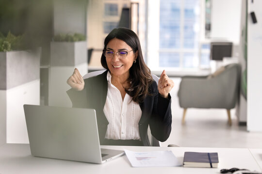 Middle-age businesswoman sits at office desk read good business news in email on laptop, closing deal, celebrate success, achievement, enjoy professional victory, got bonus, promotion or reward notice