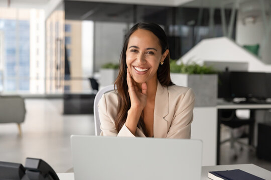Portrait of smiling Maori businesswoman or office employee sits at workplace desk with laptop, looks at camera, represents corporate success, professionalism, career growth, business goals achievement