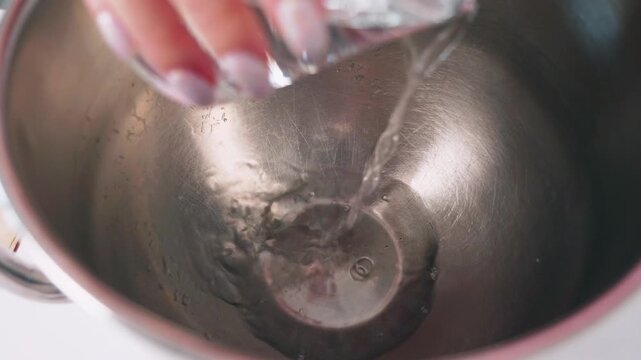 Close-up video of water being poured into a stainless steel mixing bowl during the preparation of French macarons. Baking ingredients and pastry making process in a kitchen.