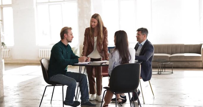 Young woman manager or team leader moderating corporate strategy meeting for diverse staff group leading brainstorming workplace discussion listening to employee feedback around table in modern office