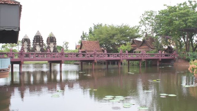 scenic view of a traditional bridge over a calm pond with historic khmer style prangs and lush greenery in thailand