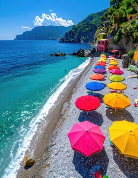 Colorful beach umbrellas line a pebbly shore next to vibrant turquoise waters and a picturesque cliffside village.