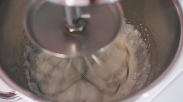 Close-up video of albumin being mixed with water in a stand mixer during the preparation of French macarons. Baking ingredients and pastry making process in a kitchen.